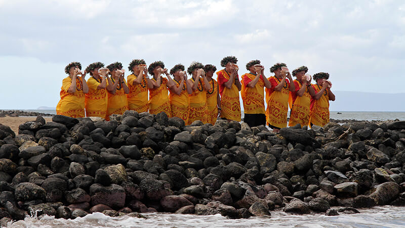 People in native Hawaiian dress blowing into conch shells