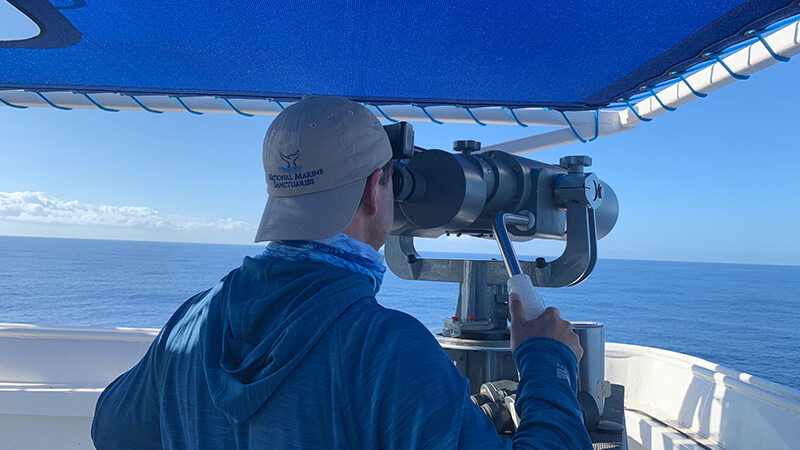 a man looks over the ocean through mounted binoculars